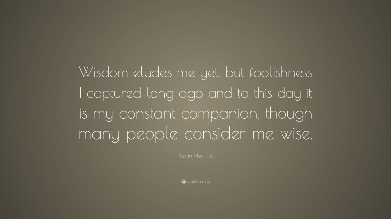 Kevin Hearne Quote: “Wisdom eludes me yet, but foolishness I captured long ago and to this day it is my constant companion, though many people consider me wise.”