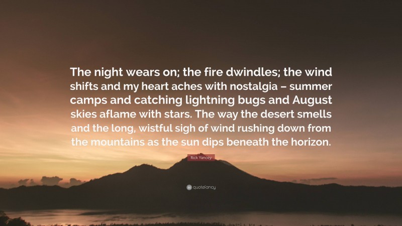 Rick Yancey Quote: “The night wears on; the fire dwindles; the wind shifts and my heart aches with nostalgia – summer camps and catching lightning bugs and August skies aflame with stars. The way the desert smells and the long, wistful sigh of wind rushing down from the mountains as the sun dips beneath the horizon.”