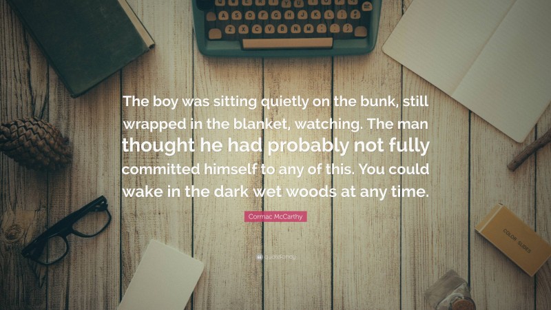 Cormac McCarthy Quote: “The boy was sitting quietly on the bunk, still wrapped in the blanket, watching. The man thought he had probably not fully committed himself to any of this. You could wake in the dark wet woods at any time.”