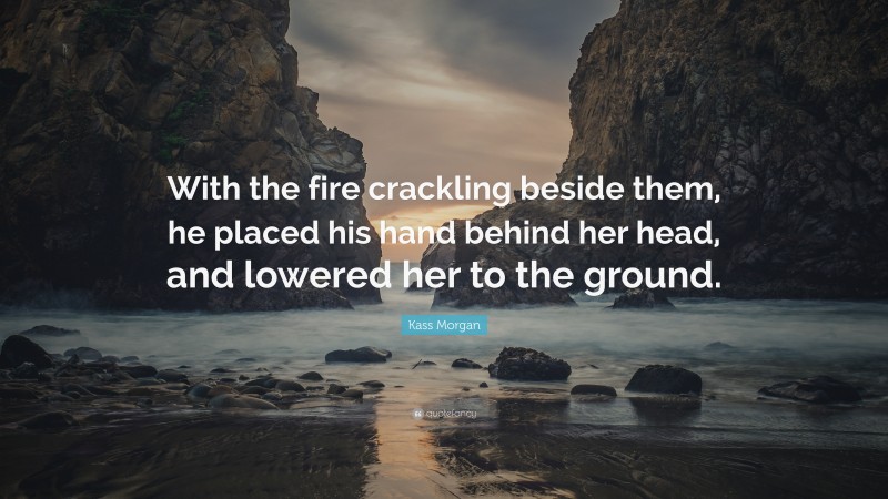 Kass Morgan Quote: “With the fire crackling beside them, he placed his hand behind her head, and lowered her to the ground.”