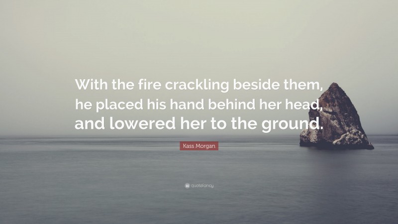 Kass Morgan Quote: “With the fire crackling beside them, he placed his hand behind her head, and lowered her to the ground.”