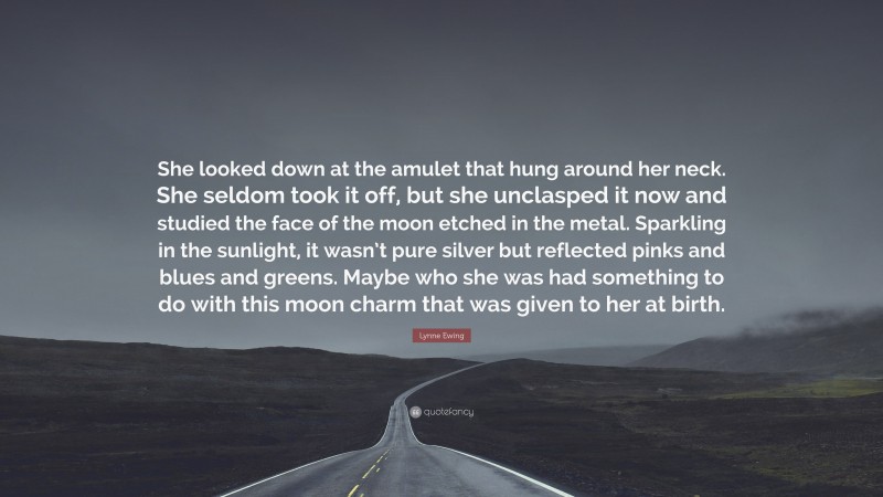 Lynne Ewing Quote: “She looked down at the amulet that hung around her neck. She seldom took it off, but she unclasped it now and studied the face of the moon etched in the metal. Sparkling in the sunlight, it wasn’t pure silver but reflected pinks and blues and greens. Maybe who she was had something to do with this moon charm that was given to her at birth.”