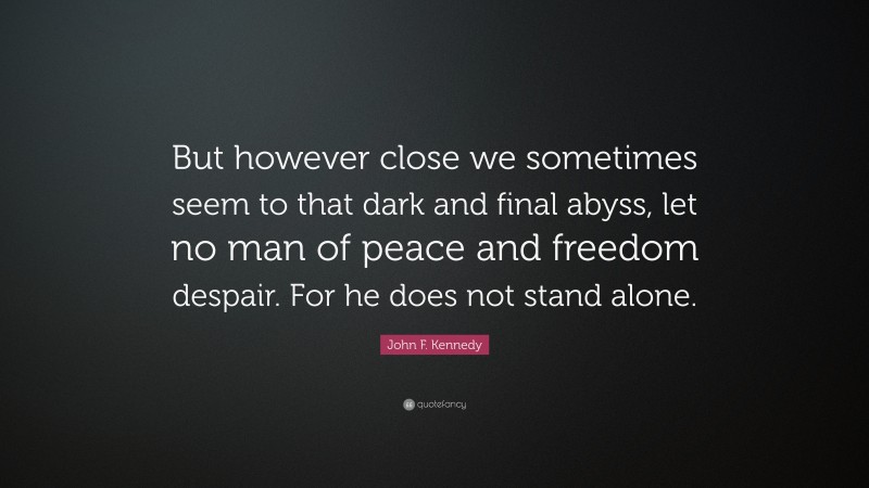 John F. Kennedy Quote: “But however close we sometimes seem to that dark and final abyss, let no man of peace and freedom despair. For he does not stand alone.”