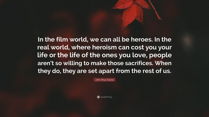 John Rhys-Davies Quote: “In the film world, we can all be heroes. In the real world, where heroism can cost you your life or the life of the ones you love, people aren’t so willing to make those sacrifices. When they do, they are set apart from the rest of us.”